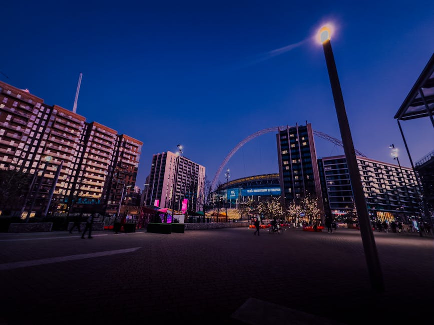 The exterior of Wembley Park Station with a large white sign displaying 'WEMBLEY PARK' mounted above the entrance, which features multiple steps leading down to the ticketing area. Several pedestrians